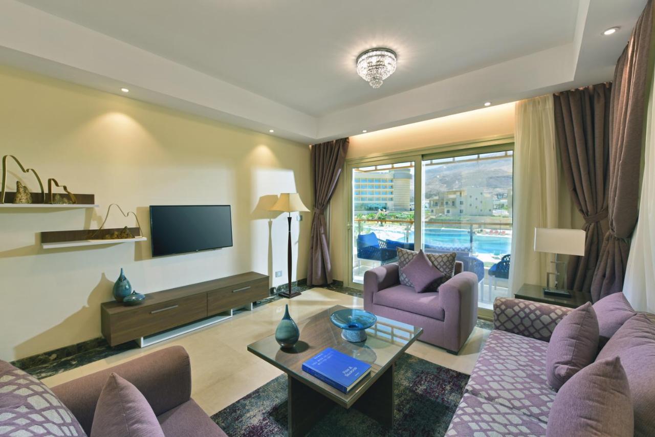 Tolip Resort El Galala Majestic Ain Sukhna Exterior foto The photo shows a modern living room that features a stylish and cozy design. There are two purple sofas with decorative cushions arranged around a coffee table. The coffee table has a blue book and a decorative item on it. A flat-screen TV is mounte