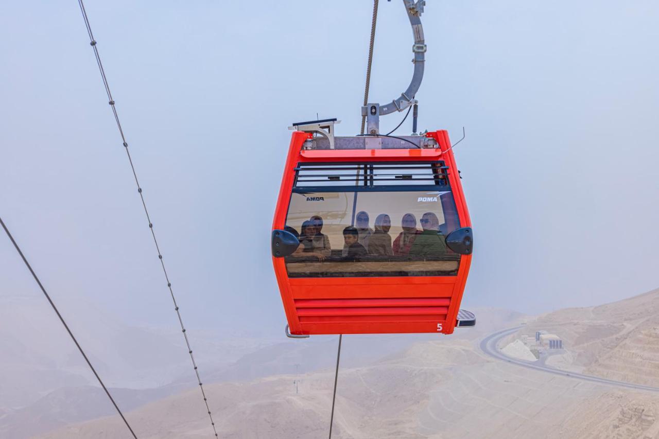 Tolip Resort El Galala Majestic Ain Sukhna Exterior foto The photo shows a red gondola lift suspended in the air, traveling along cables. Inside the gondola, a group of people can be seen. The background features a hazy landscape, possibly mountains or hills, indicating an elevated area. The scene conveys 