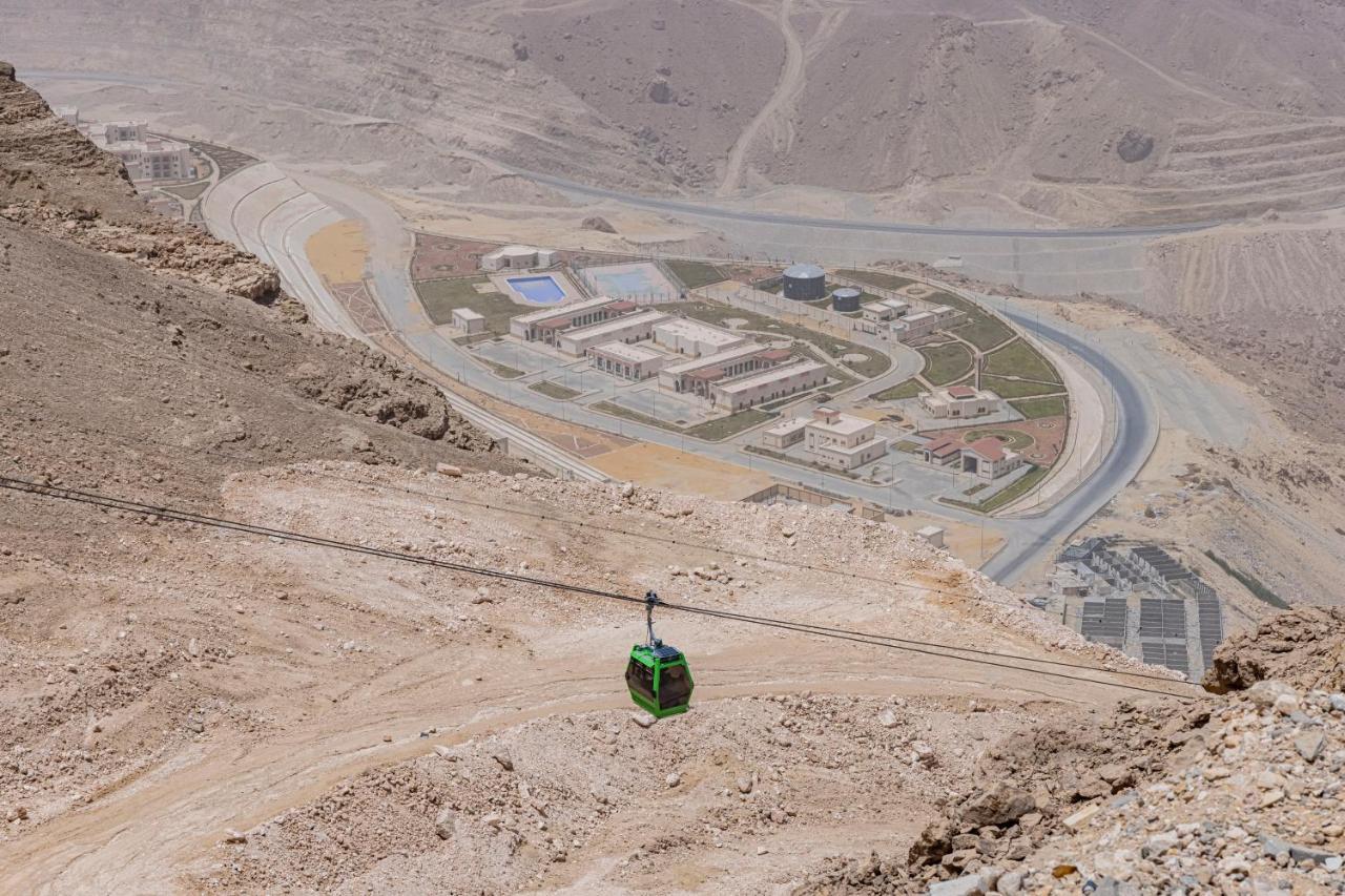 Tolip Resort El Galala Majestic Ain Sukhna Exterior foto The photo shows a mountainous landscape with a steep, dry terrain. In the foreground, there is a green cable car or gondola traveling along a cable. Below, a complex of buildings and roads can be seen, likely part of a resort or recreational area. Th