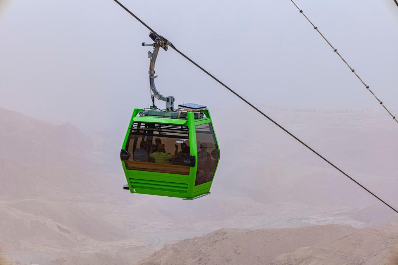 Tolip Resort El Galala Majestic Ain Sukhna Exterior foto The photo shows a green cable car suspended in the air, moving along a wire. The cable car appears to be traversing a mountainous landscape, which looks rocky and arid. The surrounding environment is somewhat foggy or hazy, suggesting limited visibil