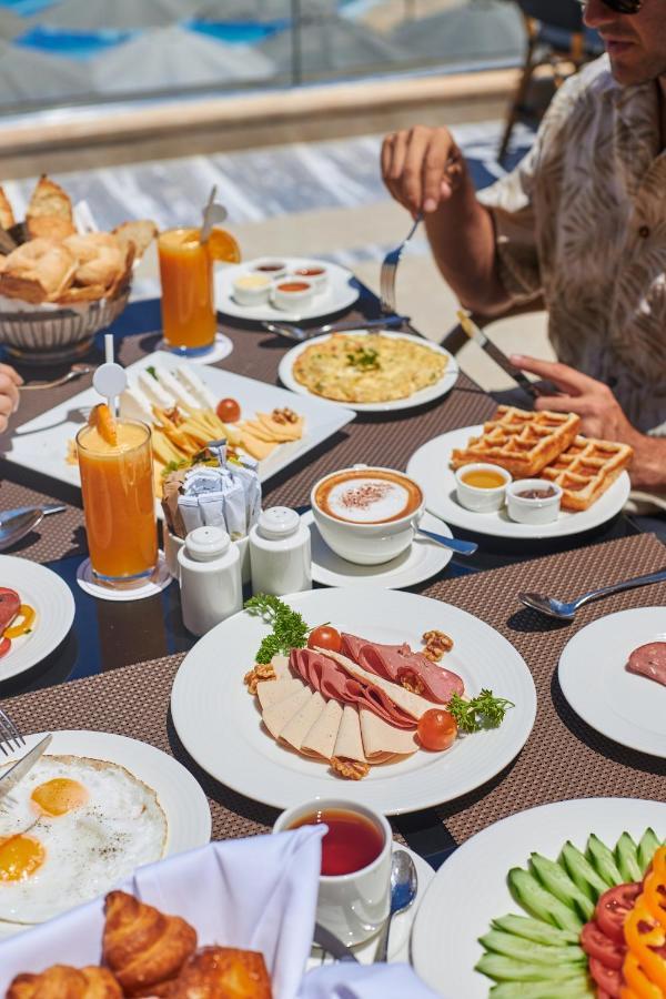 Tolip Resort El Galala Majestic Ain Sukhna Exterior foto The photo shows a breakfast spread laid out on a table. There are several plates with a variety of food items, including:

1. **Sliced Cold Cuts**: A plate featuring various cold meats, accompanied by garnishes like cherry tomatoes and lettuce.
2. **