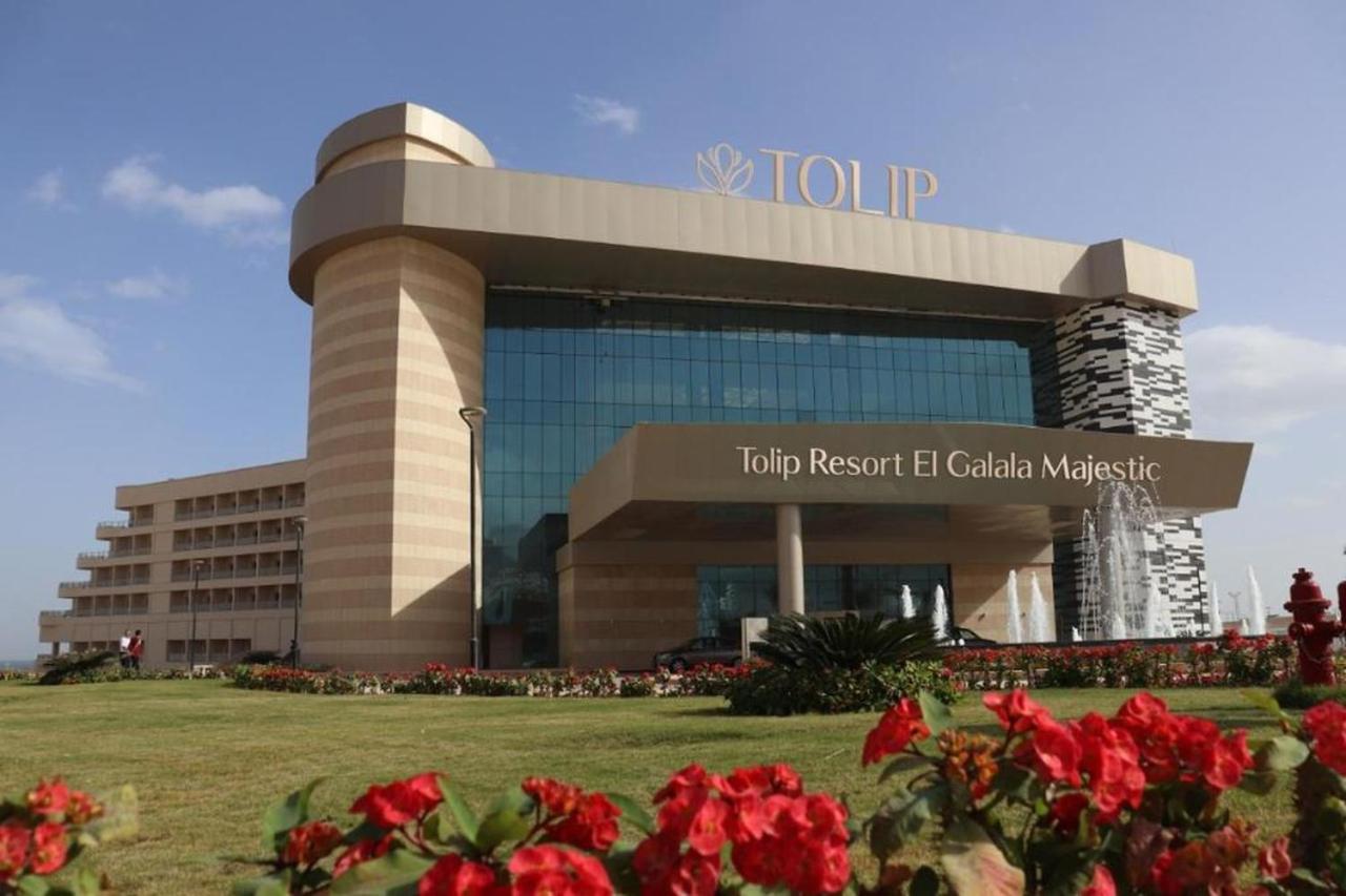 Tolip Resort El Galala Majestic Ain Sukhna Exterior foto The photo shows a modern hotel building named "Tolip Resort El Galala Majestic." The structure features a distinctive architectural design with large glass windows and a prominent entrance. Surrounding the building are well-maintained lawns and vibra