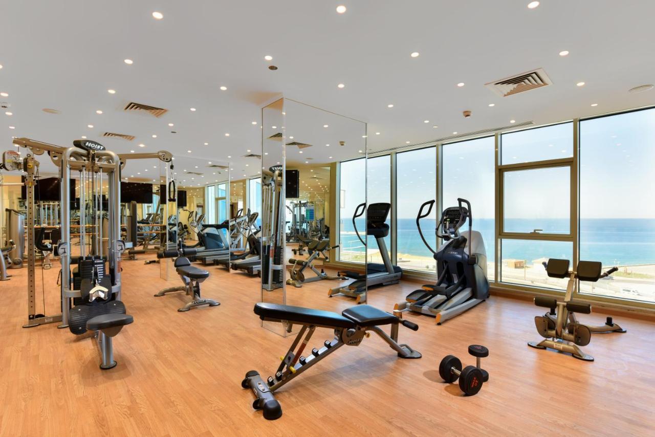 Tolip Resort El Galala Majestic Ain Sukhna Exterior foto The photo shows a modern gym interior with a variety of fitness equipment. There are cardio machines like treadmills and ellipticals, along with strength training equipment such as free weights and benches. The gym features large windows that offer a